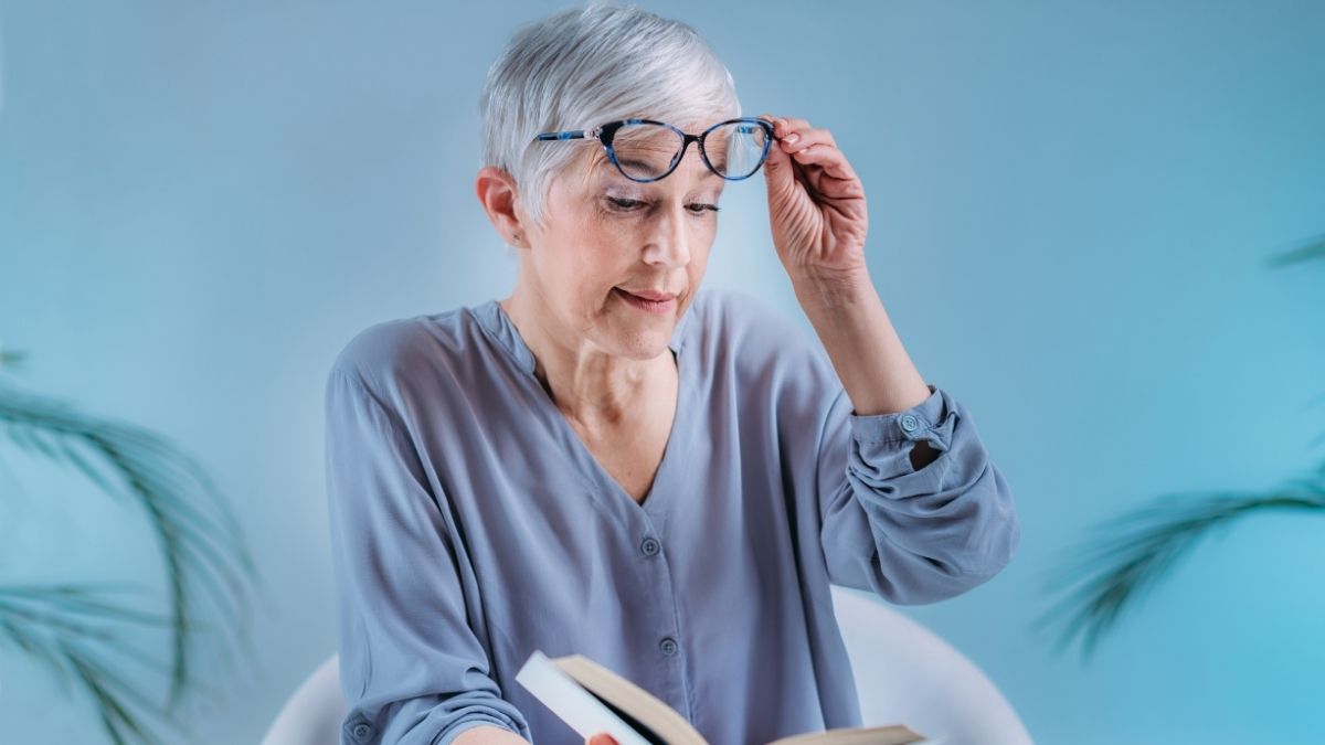 Senior woman reading a book and adjusting her glasses, illustrating the topic does medicare cover cataract removal.