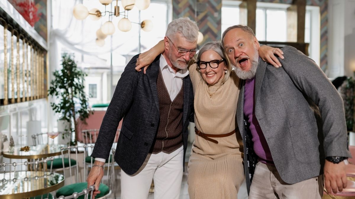Three happy seniors embracing and smiling in a stylish café, symbolizing retirement and financial security — can Medicare take your house?