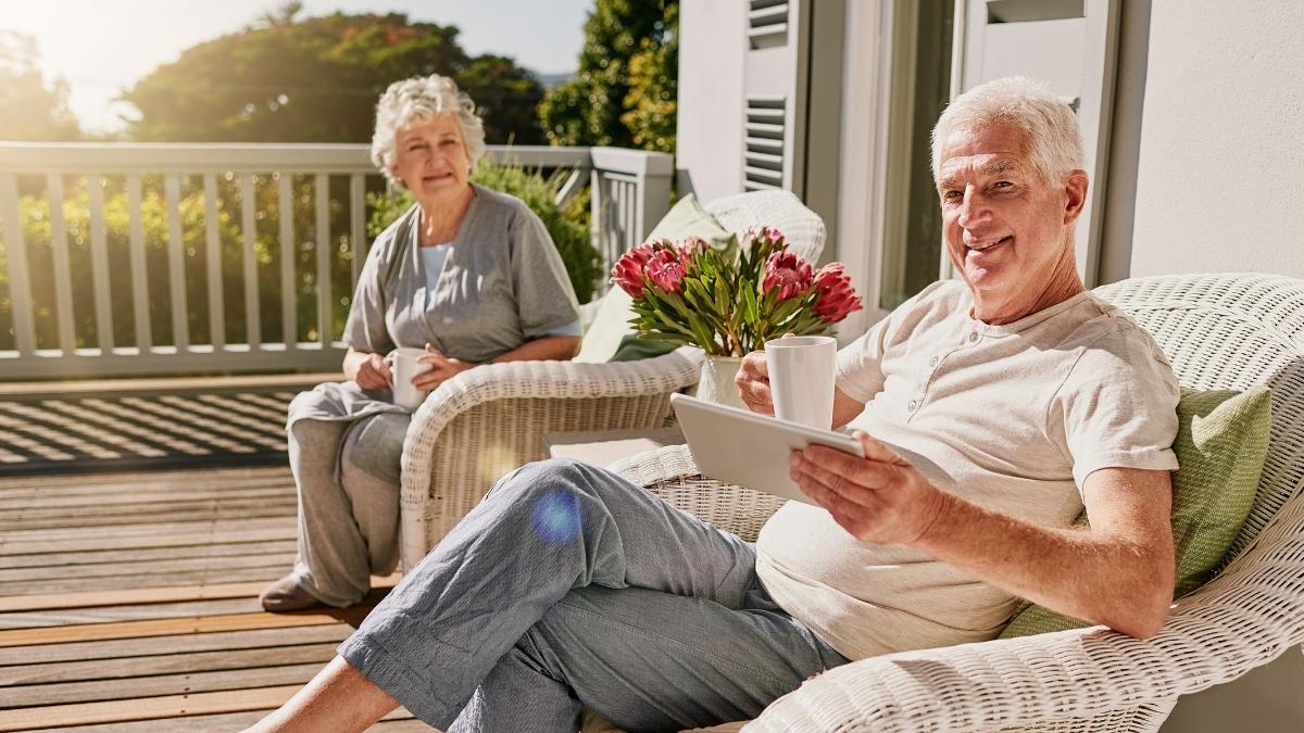 Happy retired couple relaxing on patio with coffee and tablet, exploring how to sign up for Medicare during retirement.