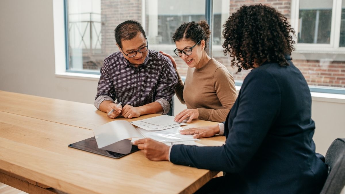 A couple reviewing financial documents with a professional advisor, discussing healthcare options such as HSA vs HRA in a modern office setting.